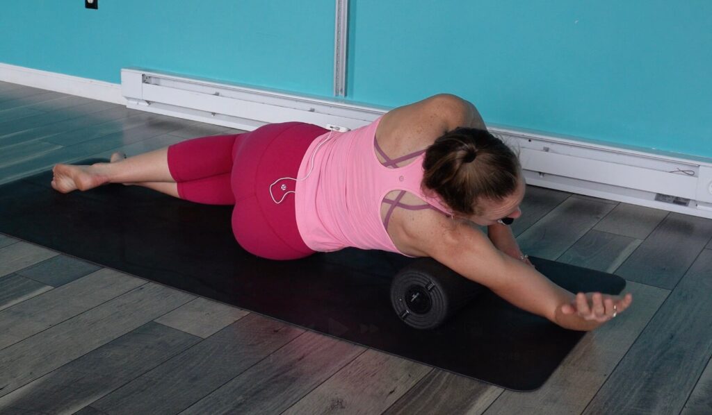 Dr. chloe laying on her right side with the foam roller under her armpit leaning onto her shoulder. She is moving her arm into external rotation as an active release technique